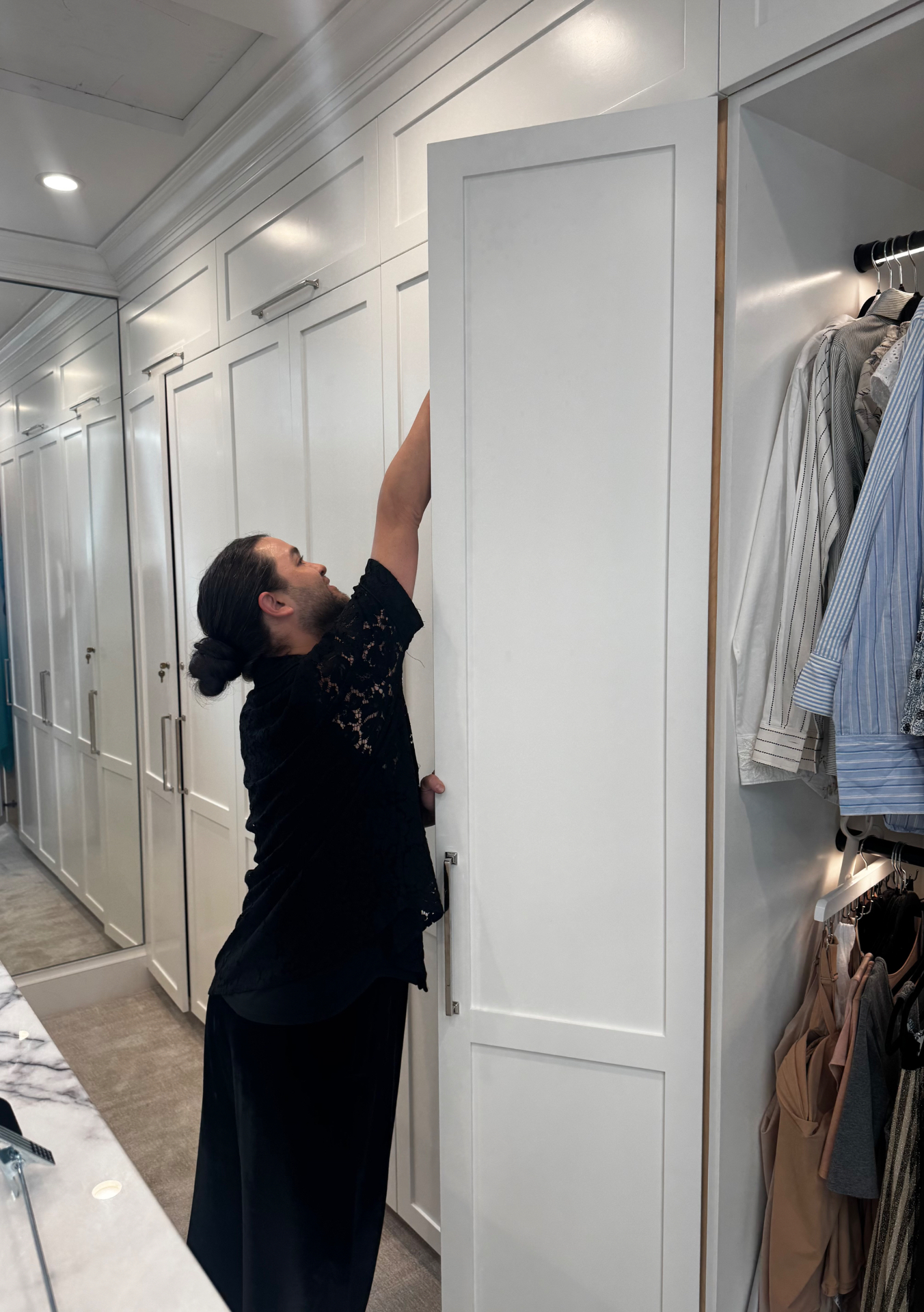 Carwin Brice reaching into a custom white walk-in wardrobe during a closet edit