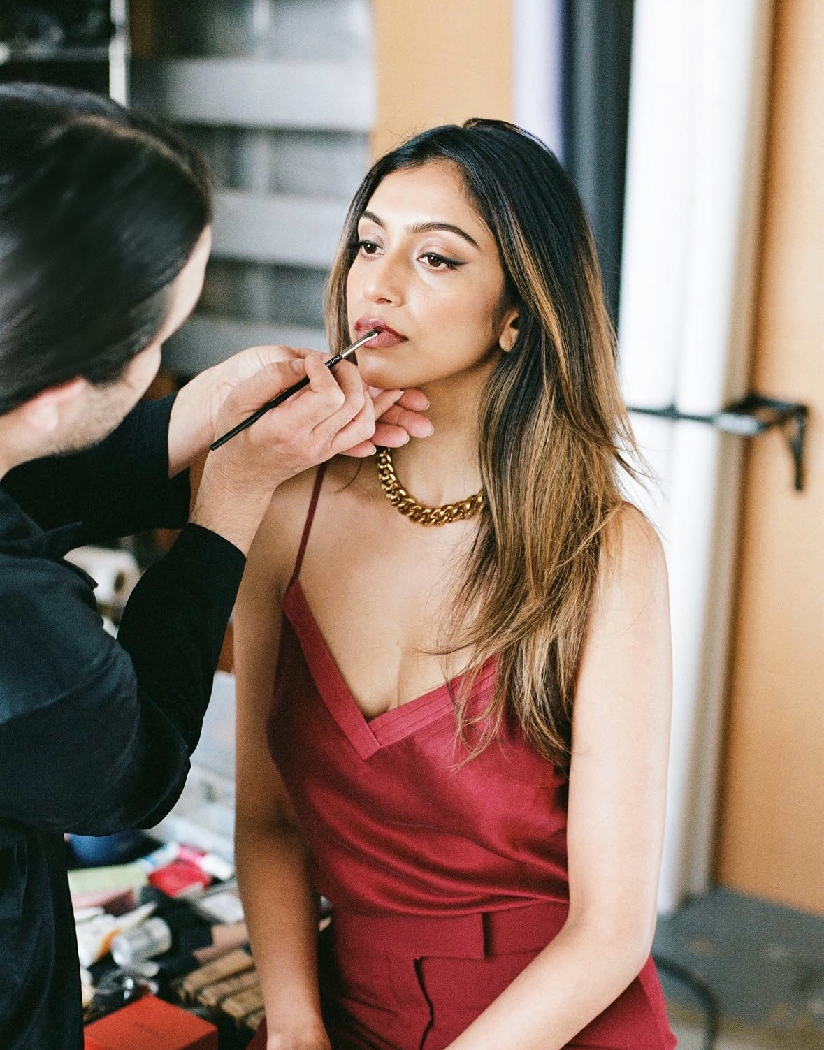 Carwin Brice applying lip color on model in red silk dress with gold chain